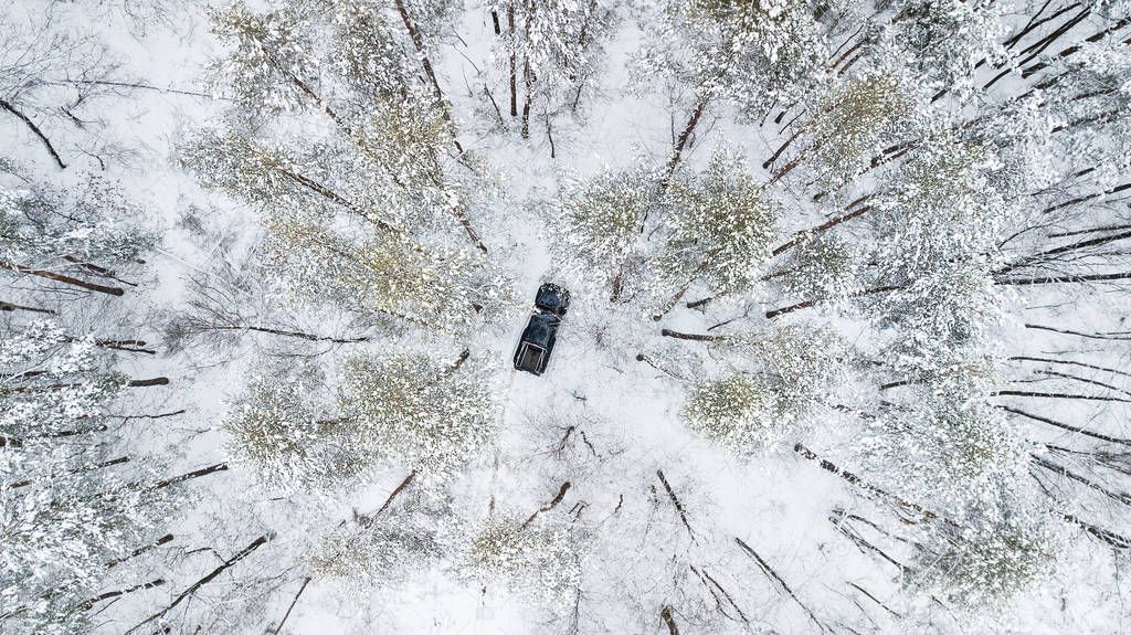 Aerial view on SUV 6x6 that rides by winter road in snow-covered forest