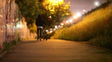 Adam şehirde gece yolu boyunca bisiklet sürüyor.