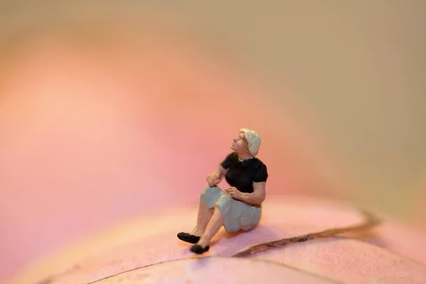 Figurina Miniatura Una Donna Sola Seduta Uno Sfondo Rosa Astratto — Foto Stock