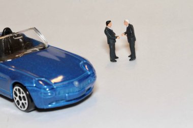 Minyatür iş adamları araba anlaşması için el sıkışıyor.