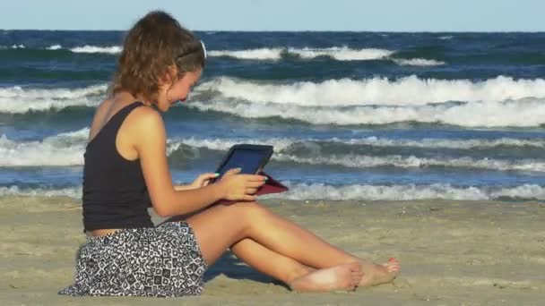 Jovem fêmea rindo duro ao ter sessão de bate-papo engraçado em seu tablet pc na praia — Vídeo de Stock