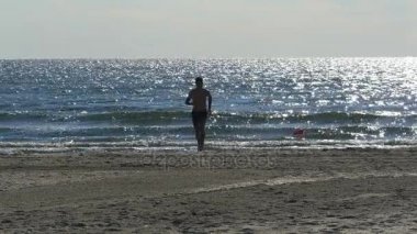 Arka plan olarak deniz ile sahilde koşan genç adam