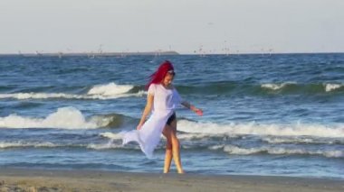 Deniz kenarında yürüyüş ve ayaklarının su ile oynarken Kızıl saçlı beyaz genç bir kadın