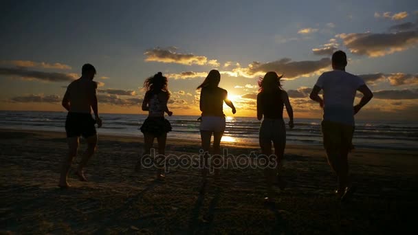 Groep van vijf vrienden samen lopend naar de zee op een strand bij zonsondergang in slow motion — Stockvideo