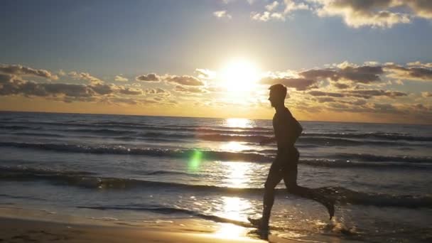 Hombre atleta haciendo ejercicio al atardecer en la playa en cámara lenta — Vídeo de stock