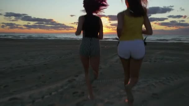 Girl friends running on the beach towards the sea at sunrise — Stock Video