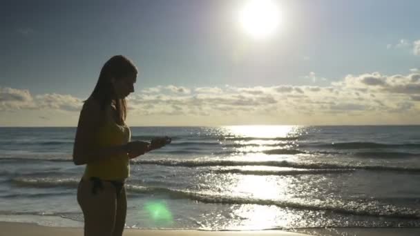Молодая женщина надевает наушники и собирается на пробежку по пляжу — стоковое видео