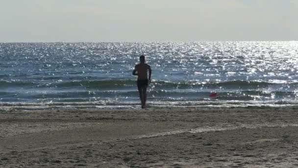A strandon, ahol a tenger a háttérben fut, fiatal férfi — Stock videók