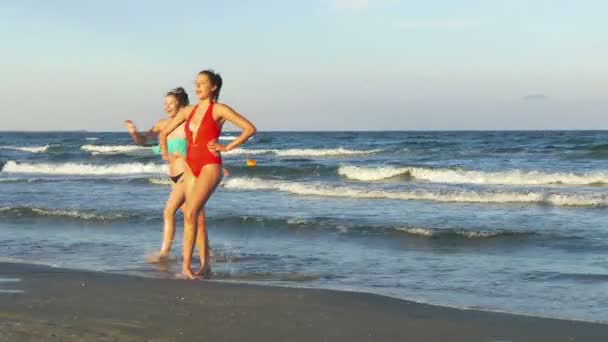 Dos hermosas mujeres jóvenes jugando en la playa y bailando — Vídeos de Stock