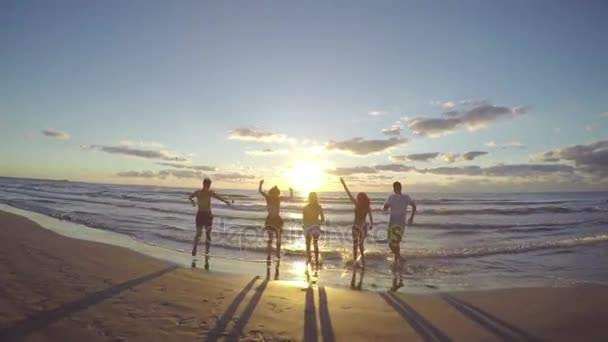 Grupo de amigos correndo em direção ao mar em uma bela praia ao nascer do sol — Vídeo de Stock