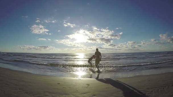 Silhueta casal provocando uns aos outros em uma praia de areia molhada — Vídeo de Stock