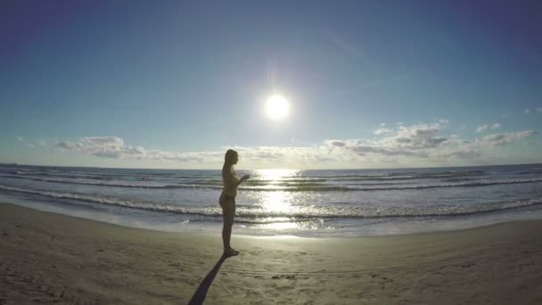 Jonge vrouwelijke zetten hoofdtelefoons en gaan voor een run op het strand — Stockvideo