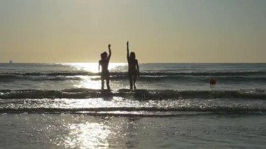 İki güzel kız eğleniyor ve okyanusun yavaş oynayan arkadaş siluetleri