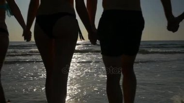 Elele ve ağır çekimde alacakaranlıkta denize doğru yürüyüş arkadaş grubu