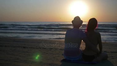 Sarılma ve öpüşme güneş doğarken sahilde oturup Romantik Çift