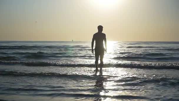 Silueta de un joven entrando en el mar en cámara lenta — Vídeo de stock