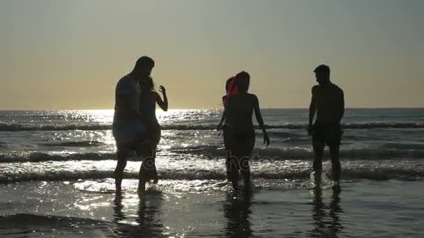 Grupo de amigos de fiesta en el océano y correr hacia la playa al atardecer en cámara lenta — Vídeo de stock