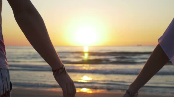 Mladý pár drží za ruce na pláži při západu slunce — Stock video