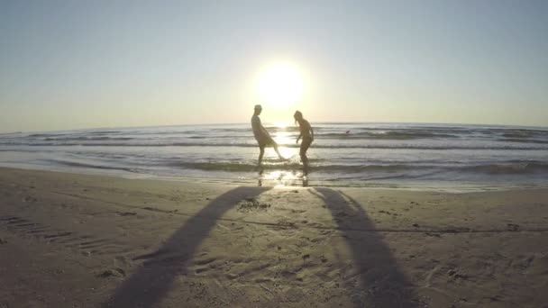 Couple silhouette playing in the sea and kissing on the beach at sunrise — Stock Video