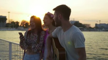 Üç arkadaş bir gitar bir köprü ile yaz saati denizde üzerinde şarkı