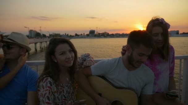 Grupo de amigos sentados en un banco y cantando en un puente sobre el mar en cámara lenta — Vídeo de stock