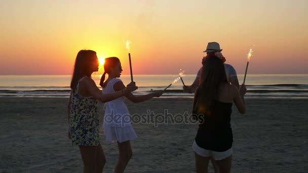 Grupo de amigos bailando con fuegos artificiales en una playa de arena al amanecer — Vídeos de Stock