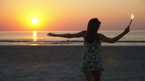 Mooie jonge vrouw dansen op een zandstrand met een vuurwerk-kaars in haar hand — Stockvideo