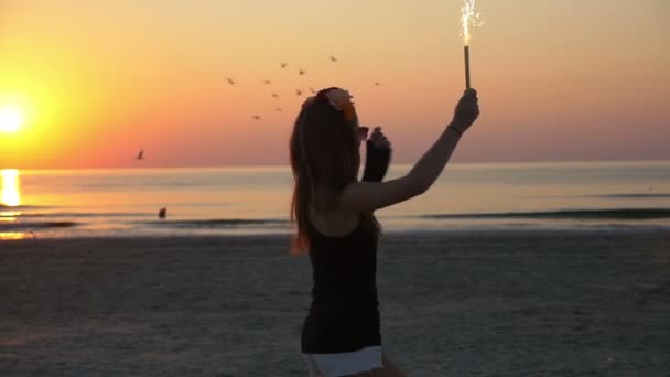 Joven hermosa adolescente hembra bailando en el crepúsculo en una playa con una vela de fuegos artificiales — Vídeos de Stock