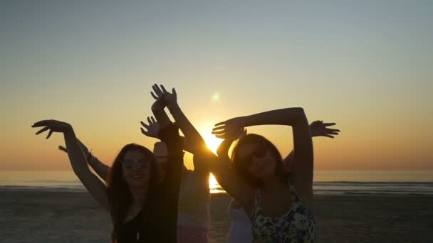 Amigos bailando felices y agitando sus manos en el aire en la playa al amanecer — Vídeos de Stock