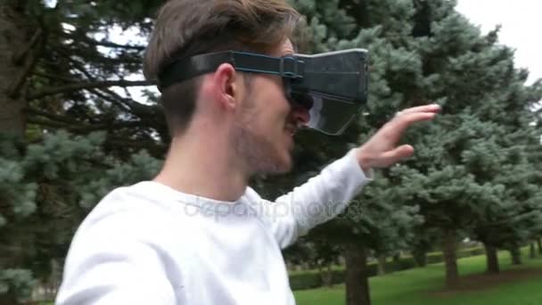 Homem vestindo óculos de realidade virtual no parque em movimento e interagindo com o mundo virtual — Vídeo de Stock