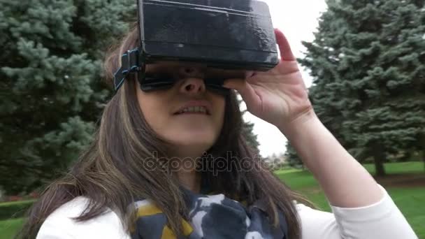 Женщина надевает наушники и смотрит вокруг на открытом воздухе в виртуальном мире — стоковое видео