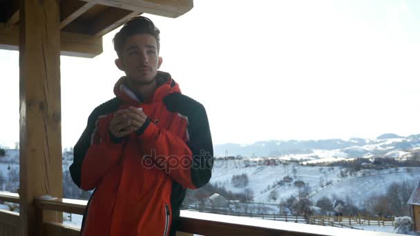 Joven bebiendo una taza de café caliente en una terraza en invierno — Vídeos de Stock