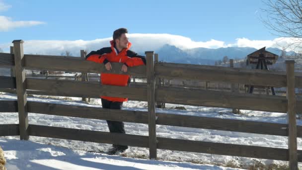 Jovem sorrindo e apoiando-se em uma cerca em um belo dia de inverno no campo — Vídeo de Stock