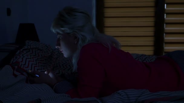 Asszony állt a szobájában az ágyon éjszakai és gördülő ő szúró telefon-on — Stock videók