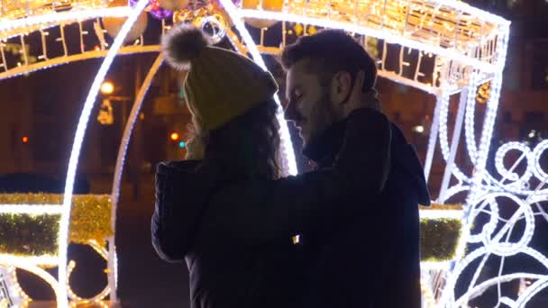 Любовники целуются и обнимаются на рождественской ярмарке в центре города ночью — стоковое видео