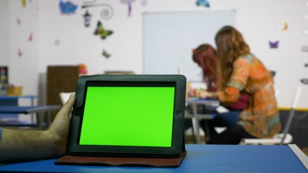 Handen på en man som håller TabletPC med grön skärm i ett kursrum — Stockvideo