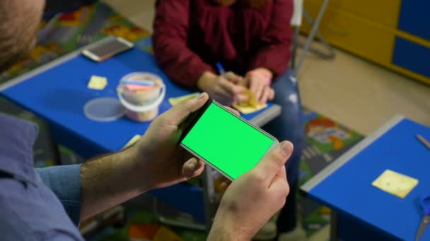 Adolescente chica escribiendo en post-it mientras que un joven está sosteniendo el teléfono inteligente con pantalla verde — Vídeo de stock