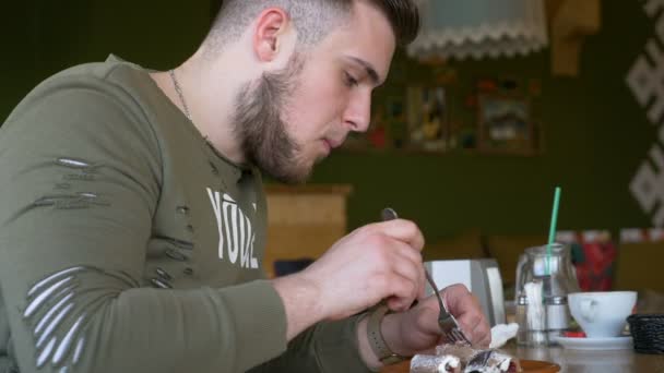 Vue rapprochée d'un jeune homme avec smartwatch manger délicieux gâteau dans un café — Video