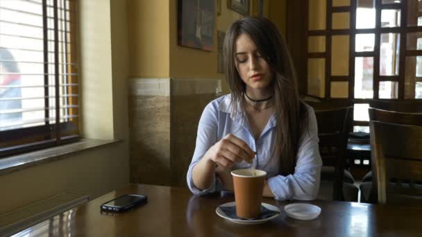 Kvinnan tittar ut genom fönstret på ett café och ta en fika på lunchrasten — Stockvideo