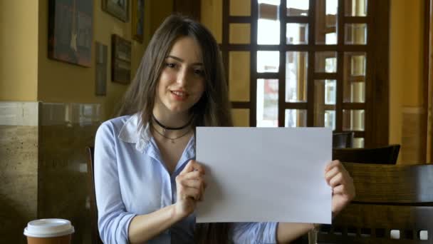 Aantrekkelijke lachende meisje houdt lege kopie ruimte witte pagina landschap georiënteerd in een restaurant-café — Stockvideo