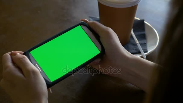 コーヒー ショップで風景モードでクロマキー グリーン画面を持つスマート フォンを見ている女性 — ストック動画