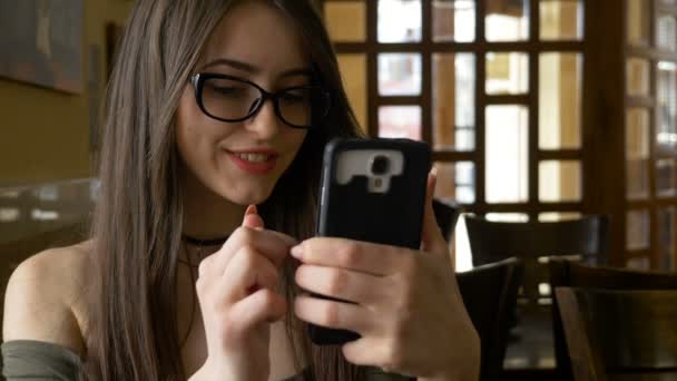 Жінка дивиться смішні відео на смартфон у соціальних мережах і прокручується в кафе — стокове відео