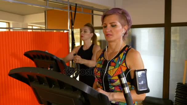 Ανώτερος γυναίκα στο γυμναστήριο χρησιμοποιώντας smartphone, ενώ το περπάτημα για την stepper και ακούγοντας μουσική — Αρχείο Βίντεο