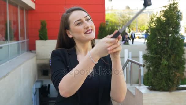 Attraktive Frau macht Gesichter und fotografiert sich mit Smartphone in der Stadt per Selfie-Stick — Stockvideo