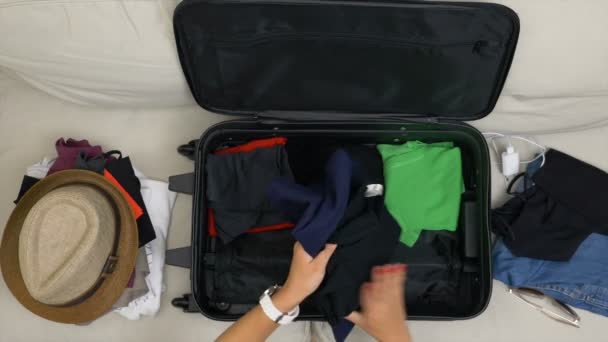 Top view of woman hands with red nails filling suitcase with folded clothes for travel trip — Stock Video