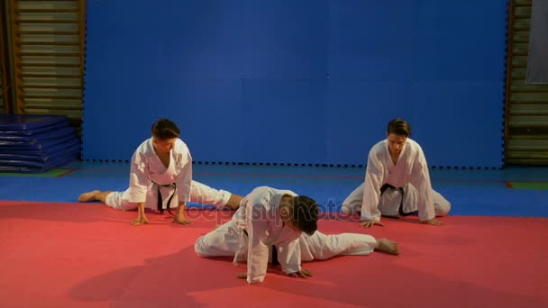 Drie jonge mannen dragen van karate kimono's uitrekkende oefeningen in de sportschool doet — Stockvideo