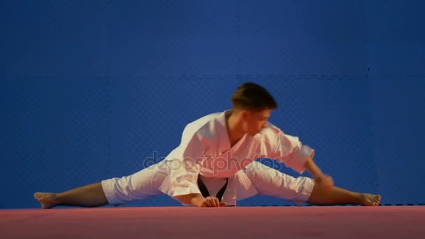 Hombre practicante de karate sentado en posición de torzal en el suelo y estirando sus músculos durante el calentamiento — Vídeos de Stock