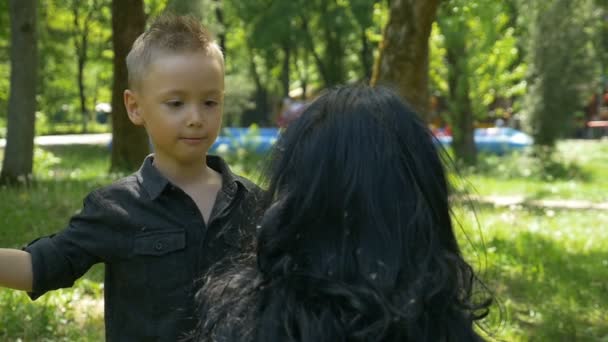 Filho bonito cuidadosamente colhendo sementes de dente de leão de cabelo escuro mãe no playground — Vídeo de Stock