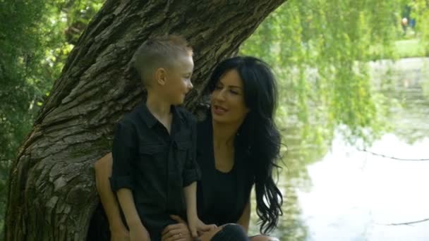 Mamă frumoasă și fiul ei drăguț se bucură de o zi frumoasă de primăvară lângă lac în parcul public — Videoclip de stoc