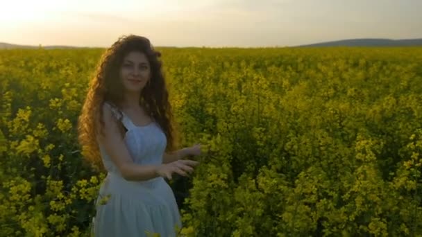 Feliz chica rizada bailando en el campo de colza disfrutando del verano al atardecer — Vídeo de stock